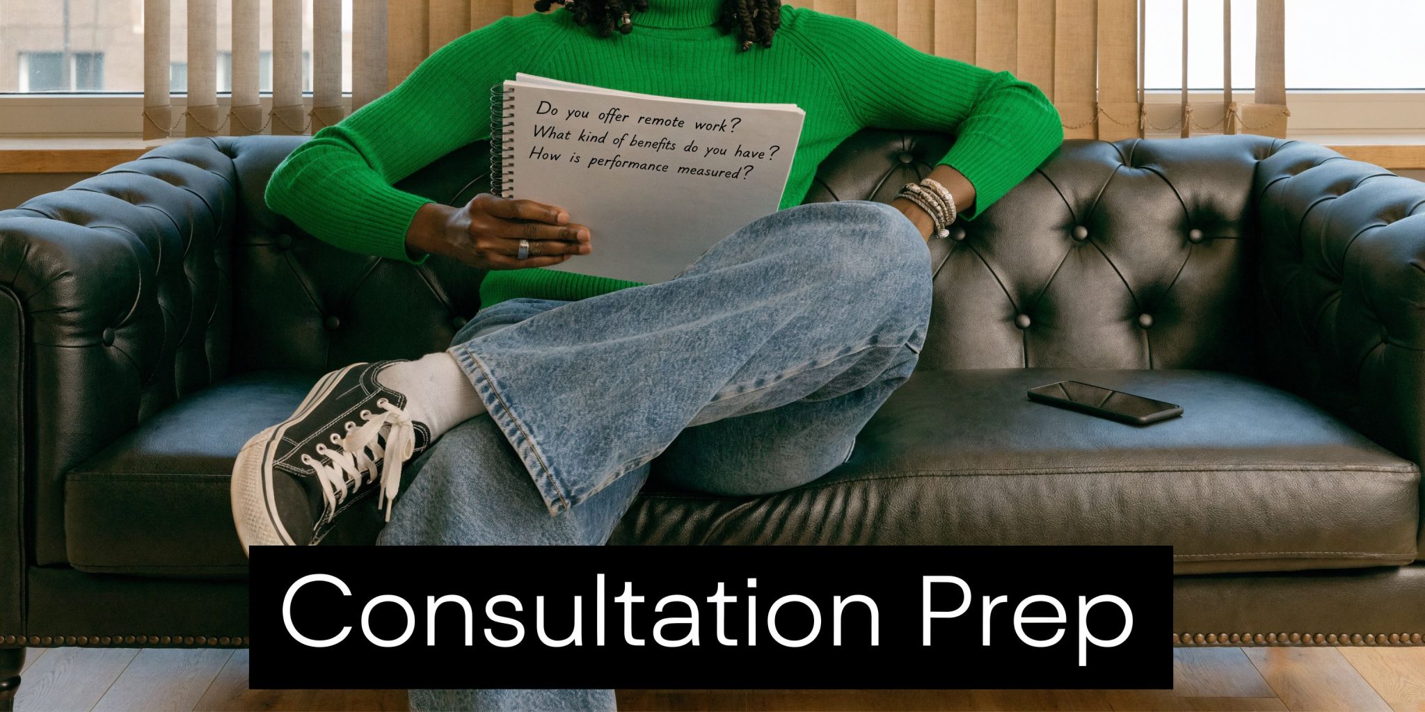A person sitting on a dark leather couch holding a notepad with questions about employment benefits.