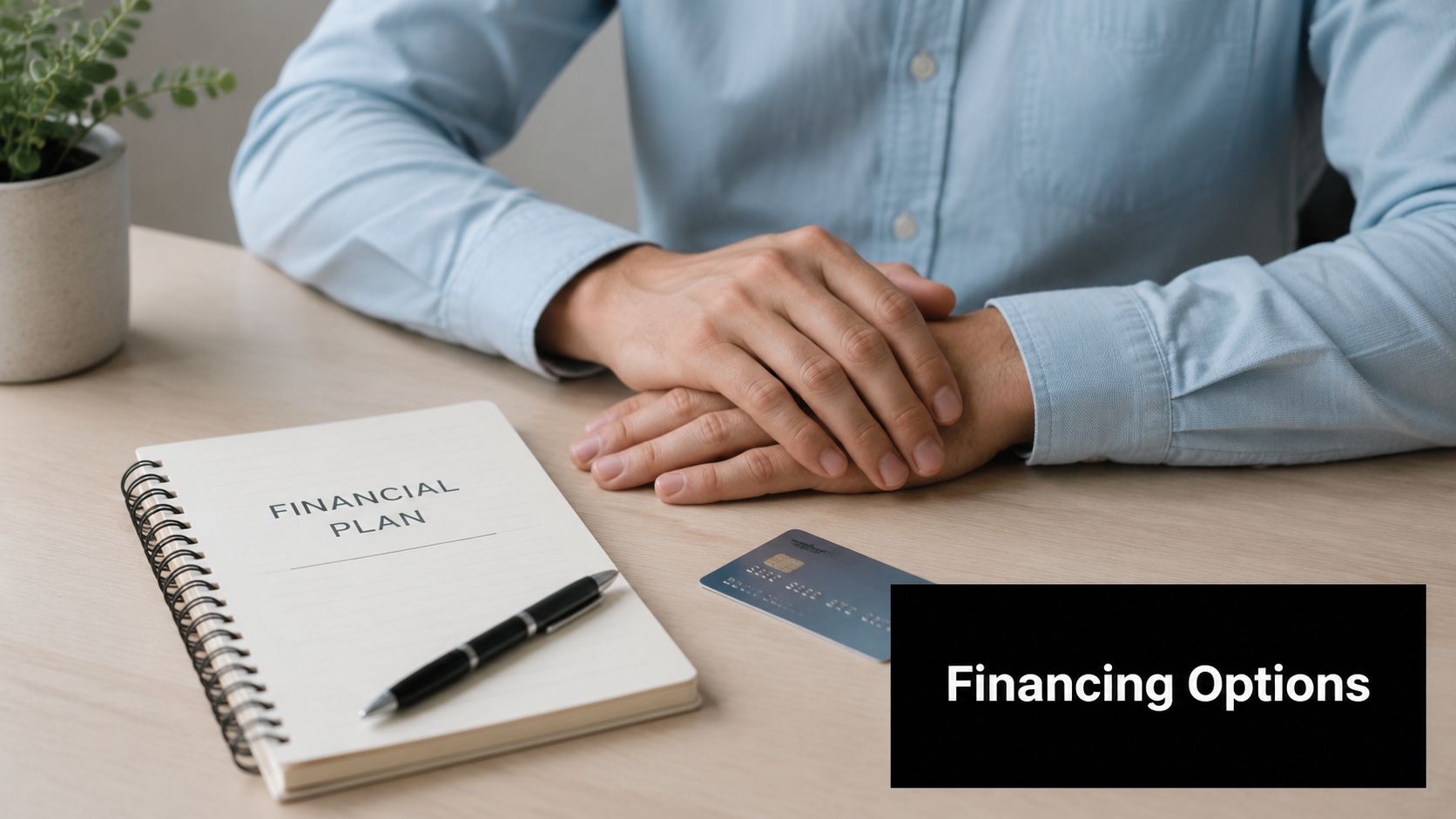 A person sitting at a desk with a notebook labeled Financial Plan and a credit card nearby.