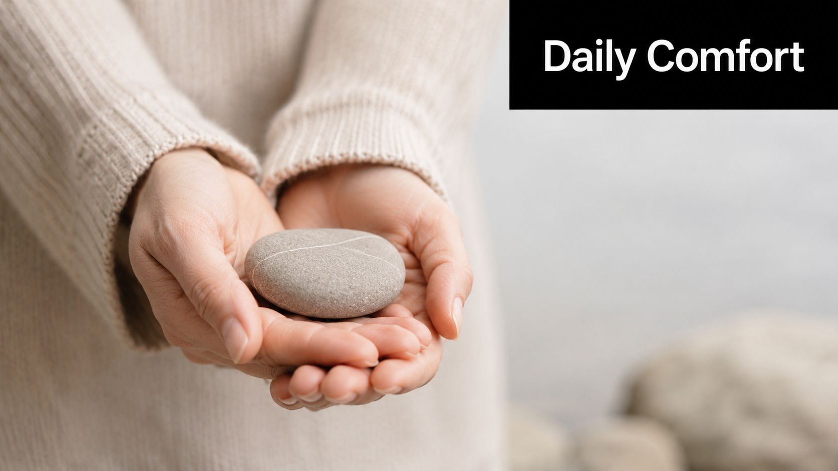 A close-up of a person wearing a cozy beige sweater holding a smooth gray pebble in their hands.