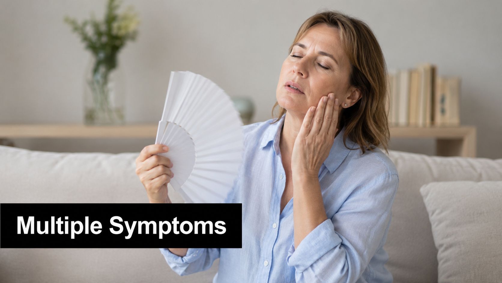 A woman experiencing menopause symptoms, holding a handheld fan while touching her face in discomfort.