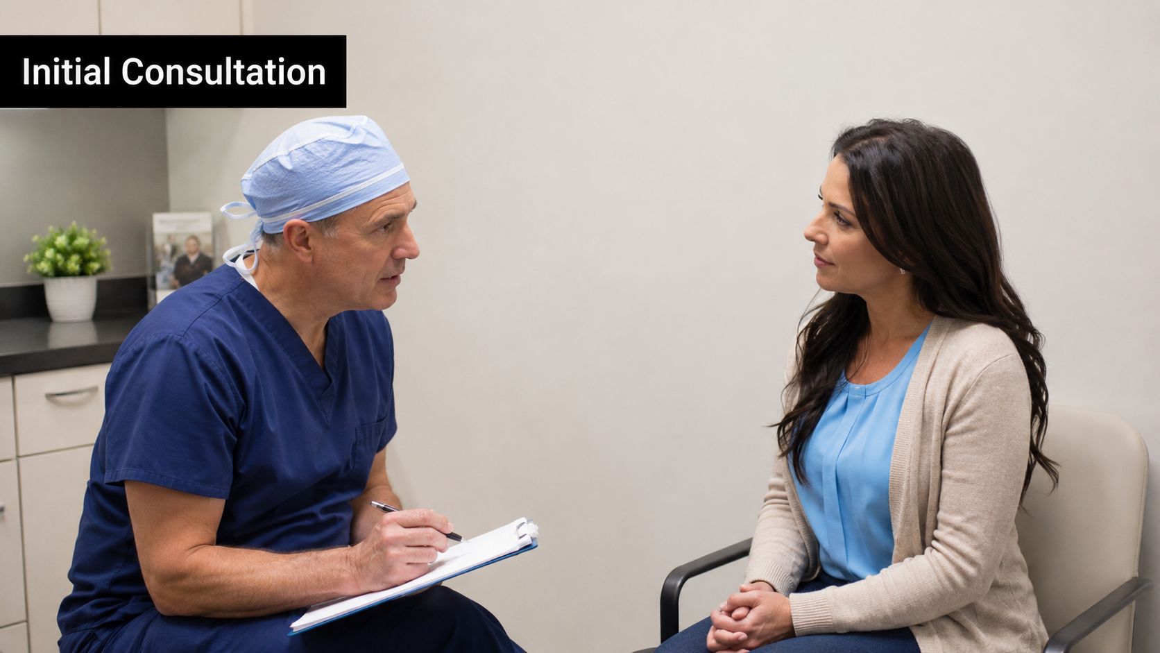 A surgeon in blue scrubs sitting and talking to a female patient during an initial medical consultation.